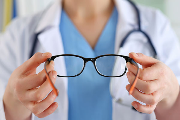Female oculist doctor hands giving pair of black glasses to patient.